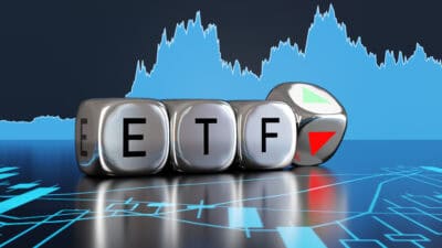 Silver metallic dice showing the alphabets ETF and an up and down arrow on backgrounds of stock charts.