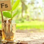 A glass outdoors with a sign with ETFs written on it, as well as coins and a growing plant.