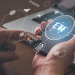 Man holding a smartphone with a hologram of the word ETF along with finance-related images.