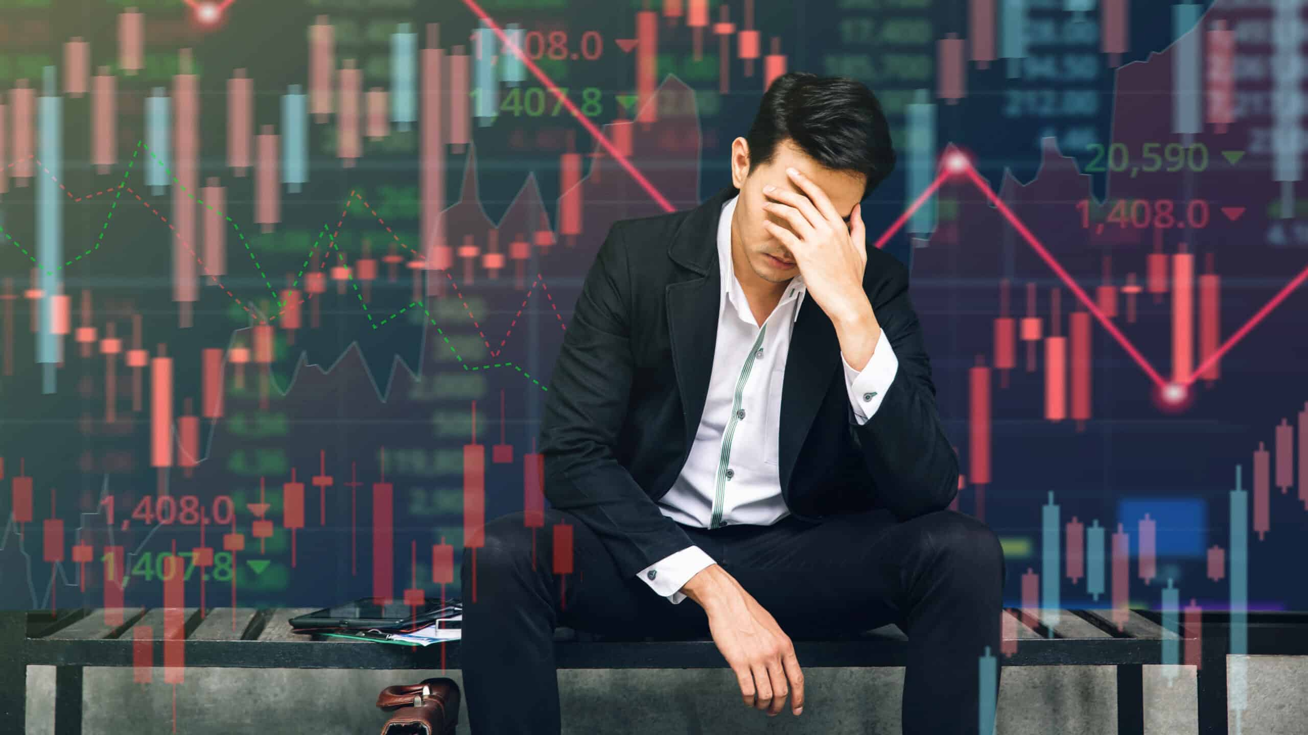 Stressed businessman sits in panic amid digital stock market financial background.