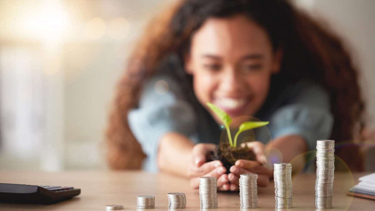 Happy girl holding a plant and soil in front of ascending piles of coins.