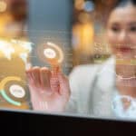 Woman pointing to a hologram of a world map with finance graphs and related themes.