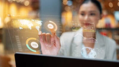 Woman pointing to a hologram of a world map with finance graphs and related themes.