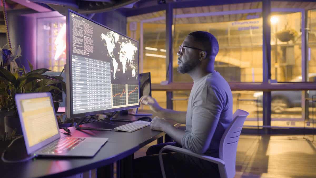 Man working on a big screen which is displaying global information about stocks with data.