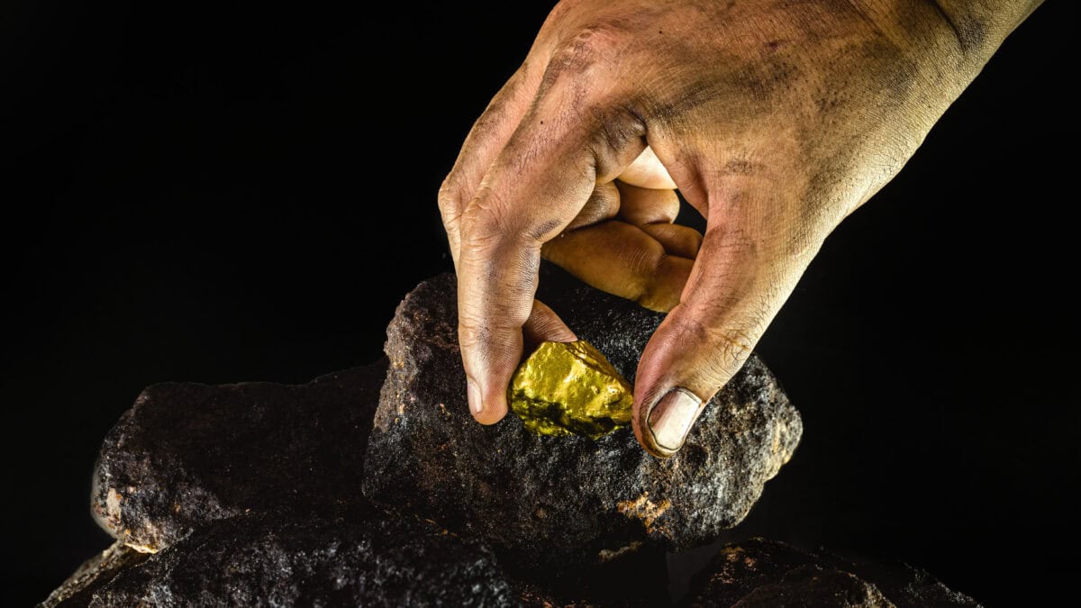 Gold nugget in a miner's hand amid black rocks.