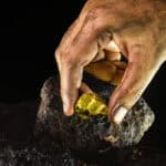 Gold nugget in a miner's hand amid black rocks.