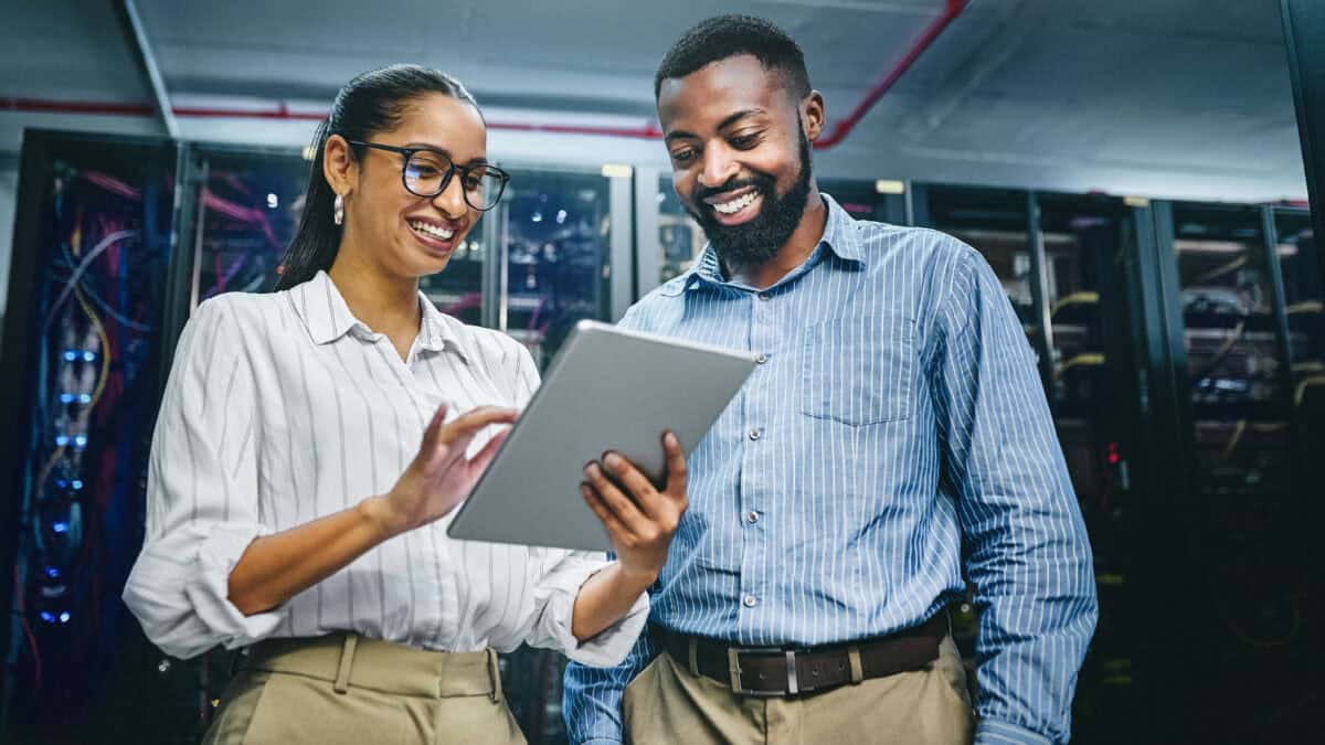 Two smiling colleagues looking at a tablet in a data centre.