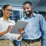 Two smiling colleagues looking at a tablet in a data centre.