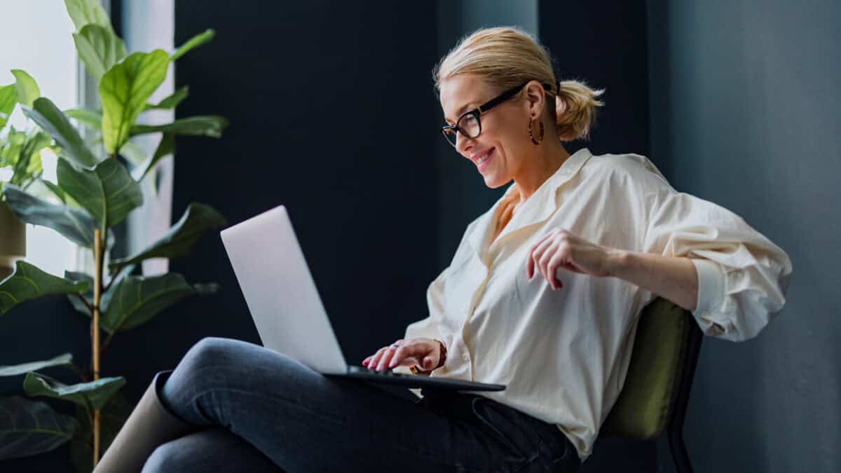 Cheerful smiling businesswoman sitting on a chair and typing business report on a laptop keyboard.