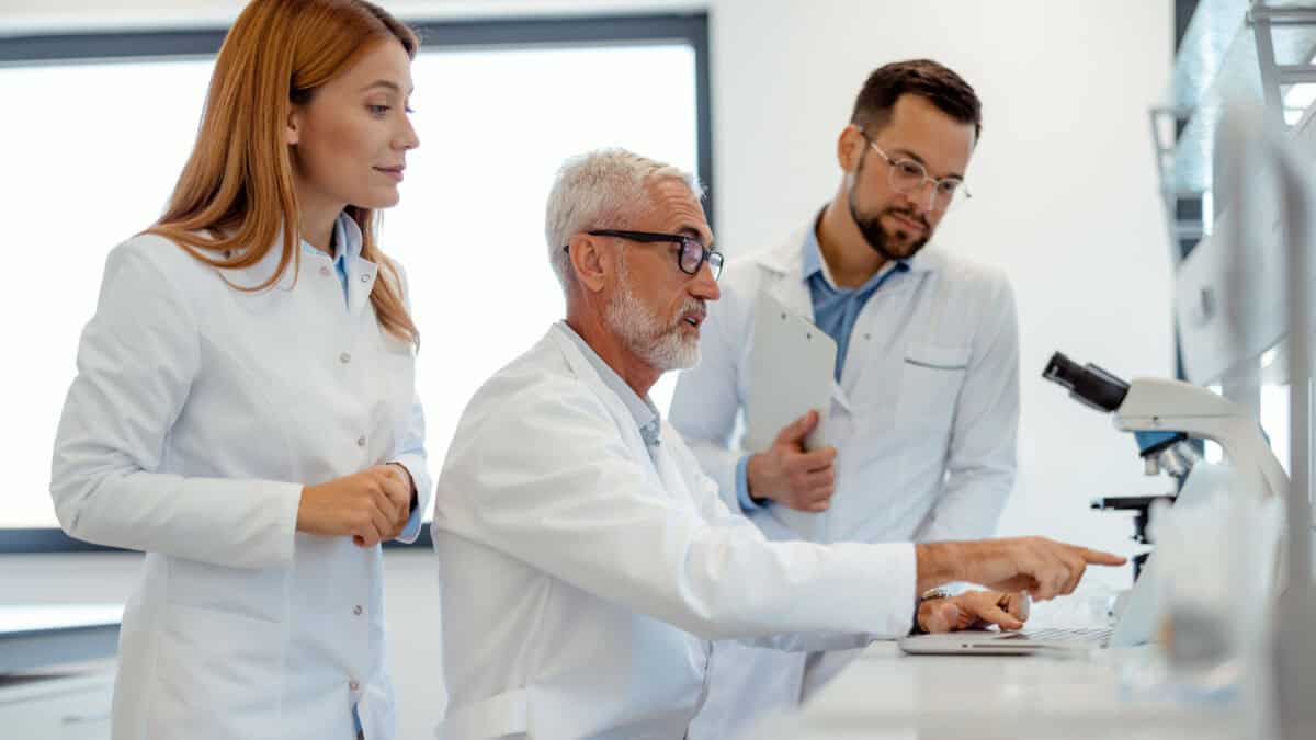 Three scientists looking at a laptop in a lab.