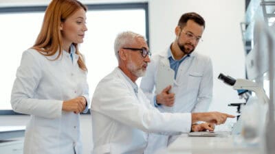 Three scientists looking at a laptop in a lab.