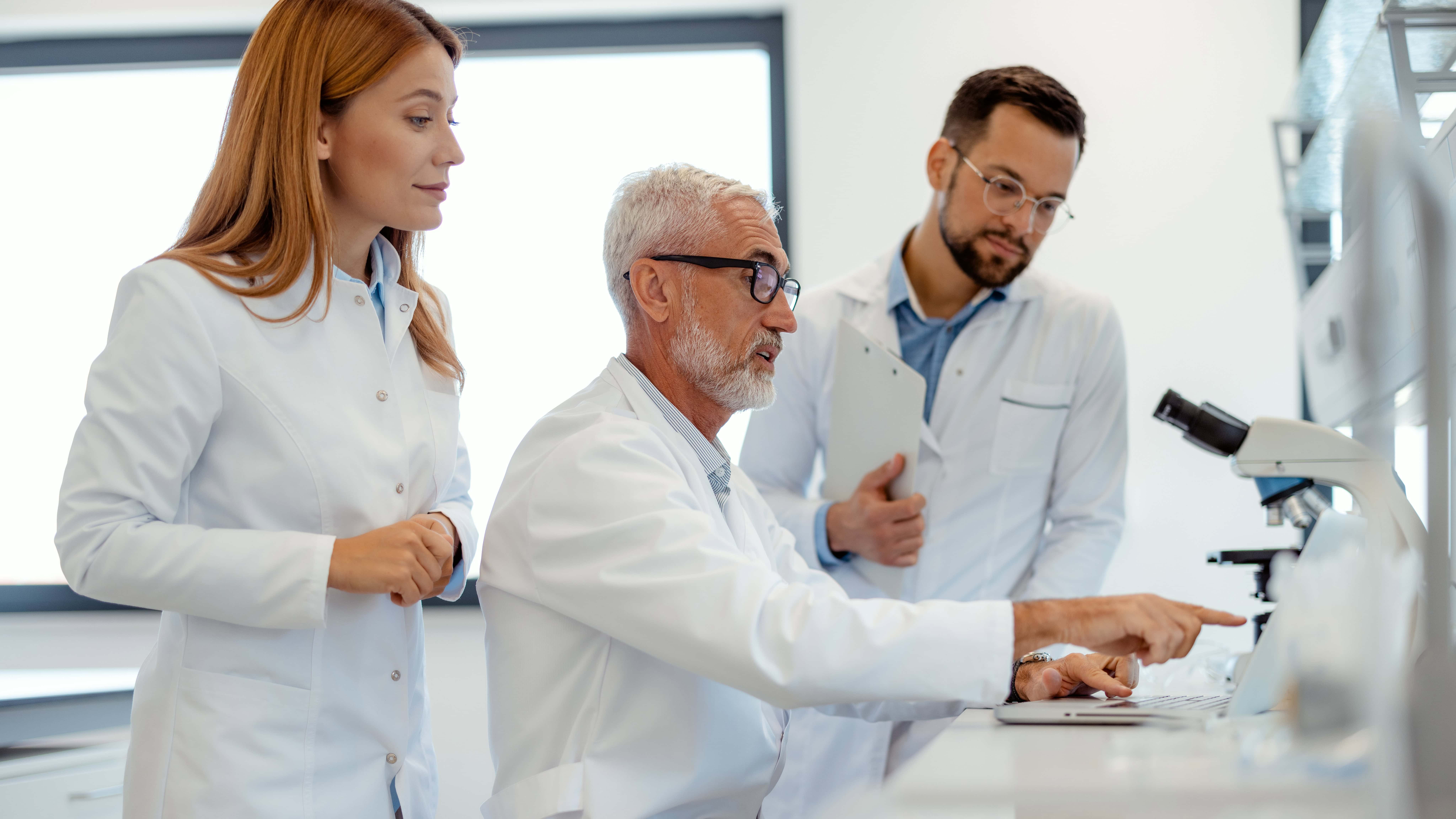 Three scientists looking at a laptop in a lab.