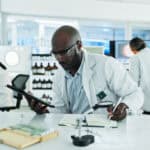 Scientist taking down notes from a tablet, with two other scientists working in the background.