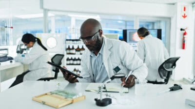 Scientist taking down notes from a tablet, with two other scientists working in the background.