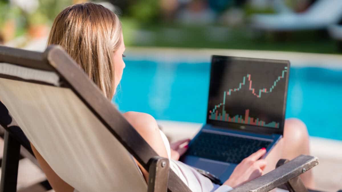 Woman sitting on a chair by the pool on her laptop, looking at a stock market chart.