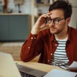 Man with hand to his forehead looking at his laptop.