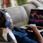 Man lying down on sofa and trading on his laptop.