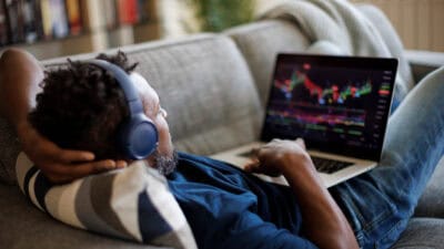 Man lying down on sofa and trading on his laptop.