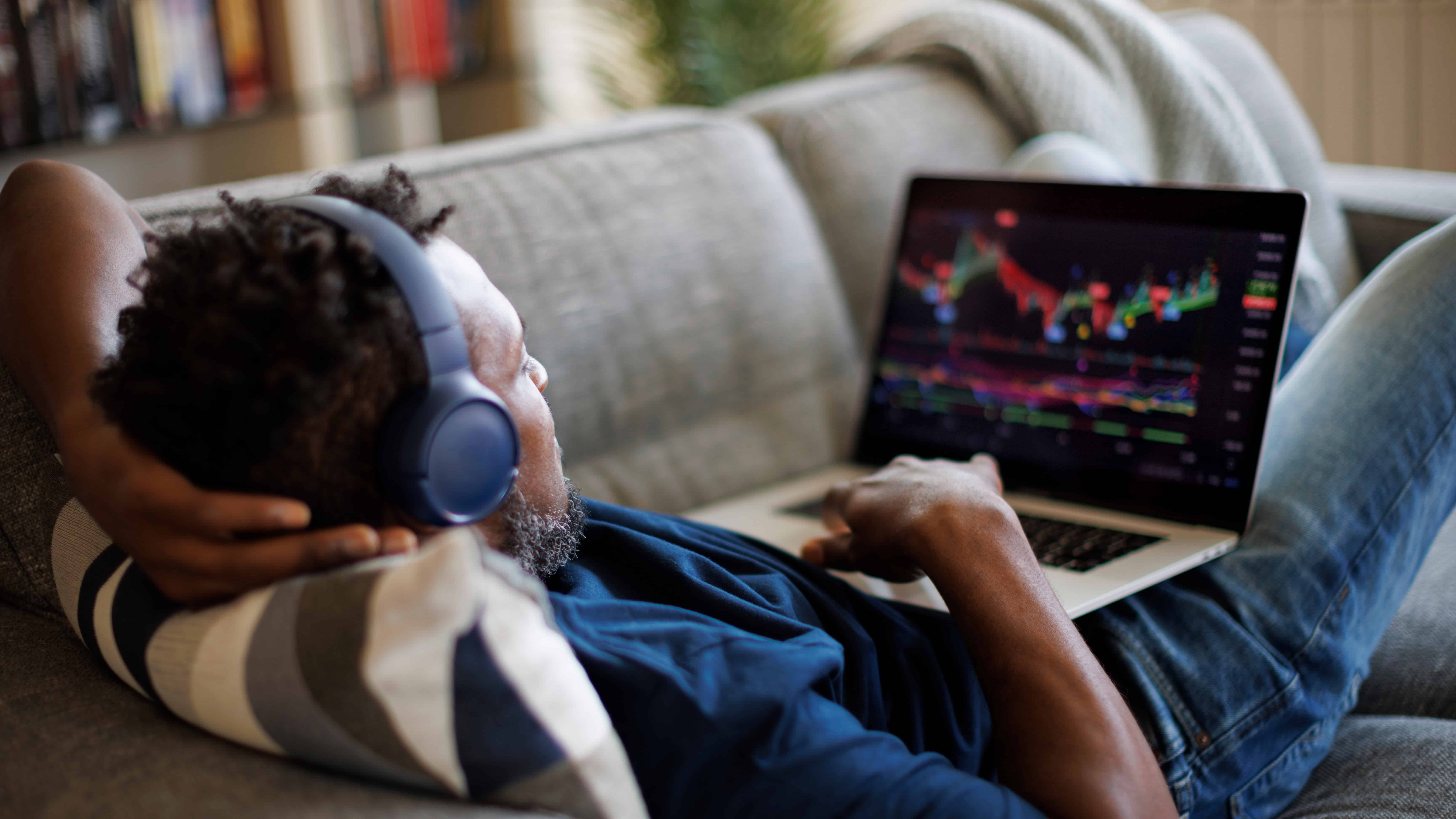 Man lying down on sofa and trading on his laptop.