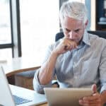 Businessman at his desk, looking seriously at information on his digital tablet.