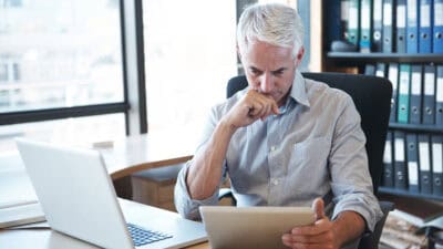 Businessman at his desk, looking seriously at information on his digital tablet.