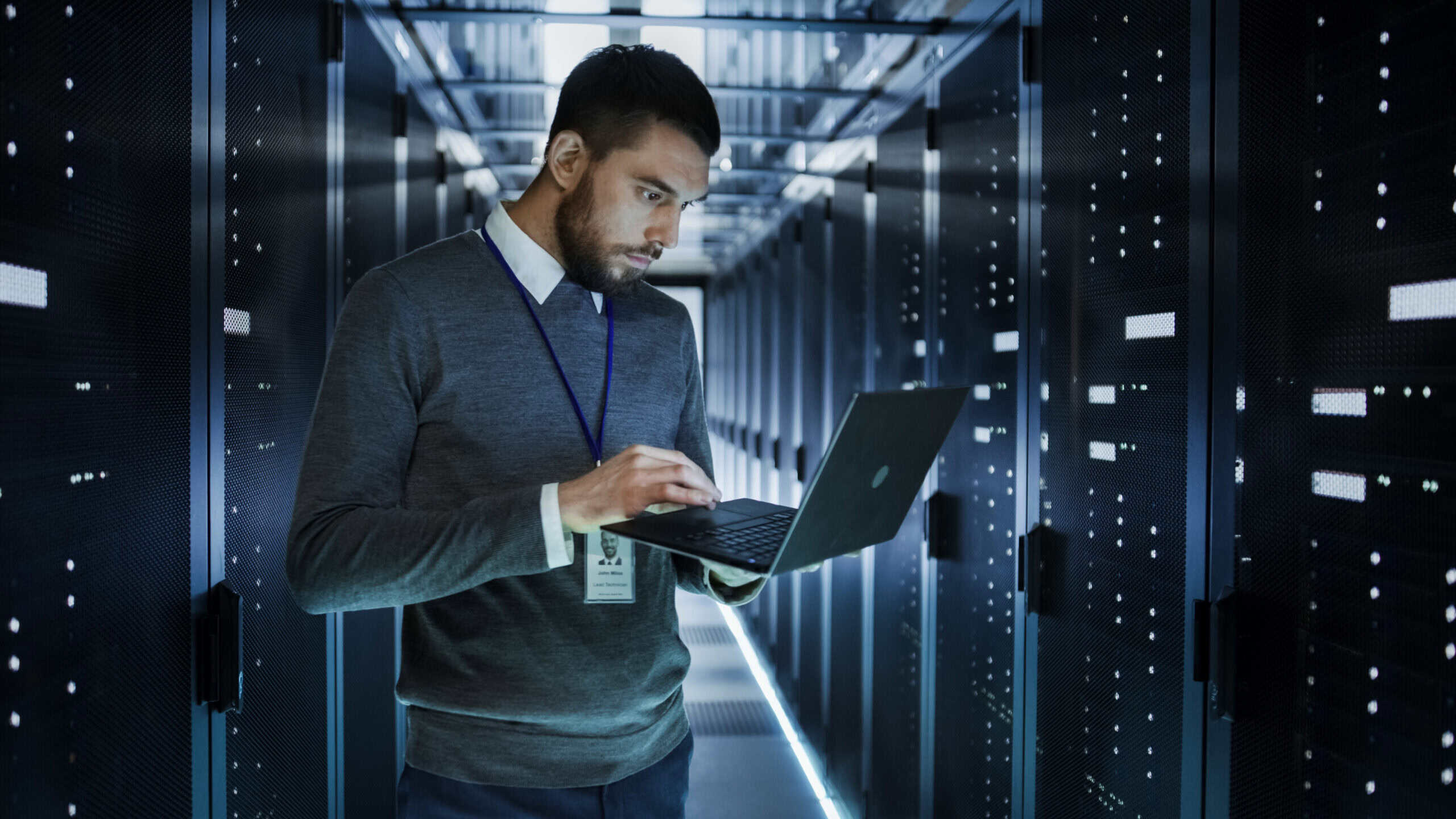 IT technician works on a laptop in big data centre full of rack servers.