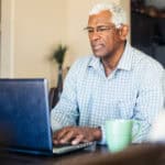 Man typing on his laptop with a coffee mug at the side.