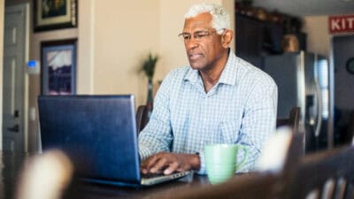 Man typing on his laptop with a coffee mug at the side.