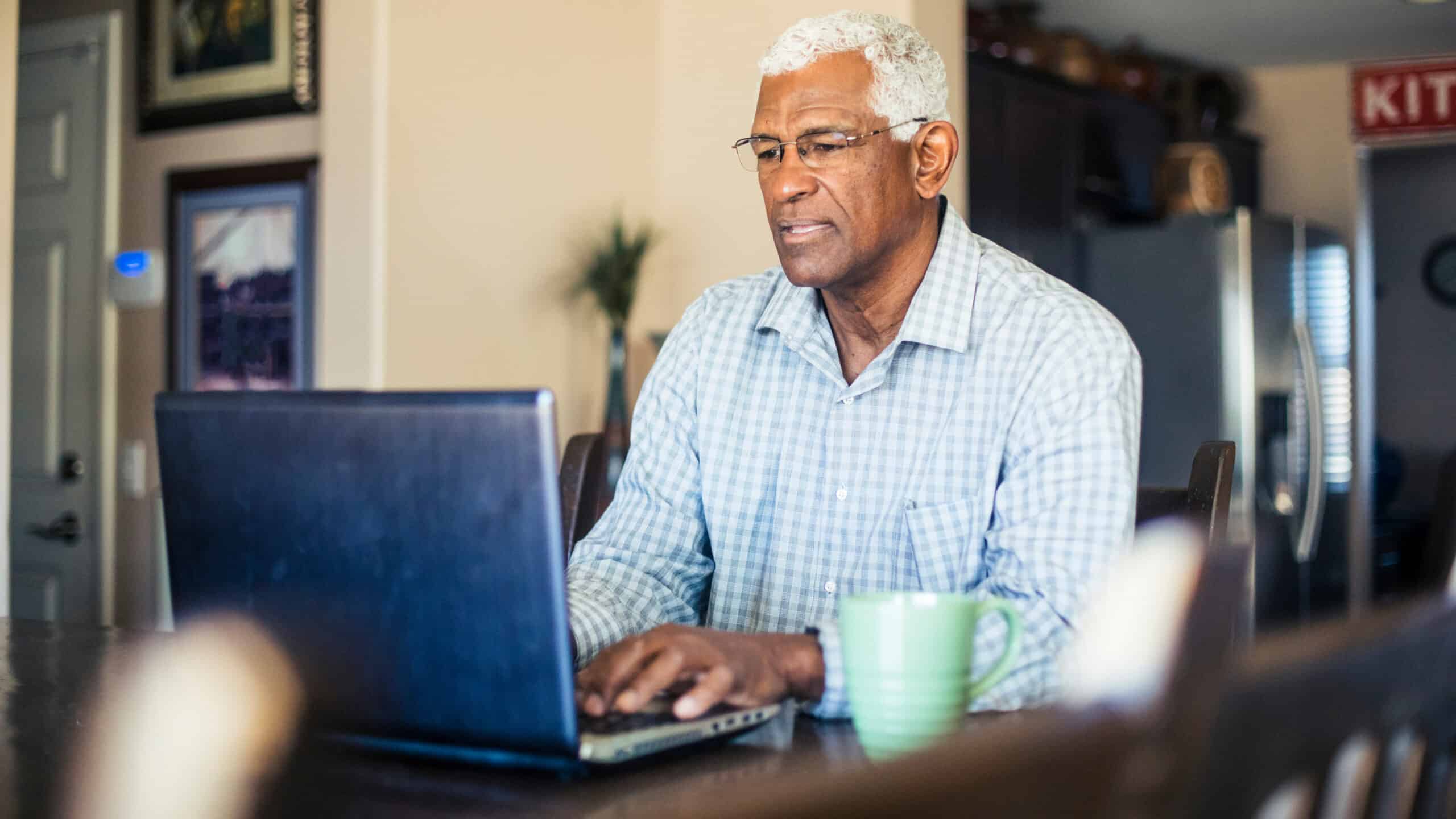 Man typing on his laptop with a coffee mug at the side.