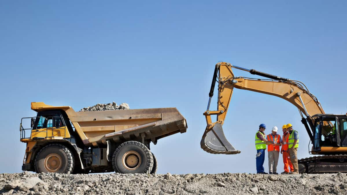 Four miners discussing with each other next to mining machinery.
