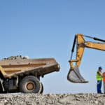 Four miners discussing with each other next to mining machinery.