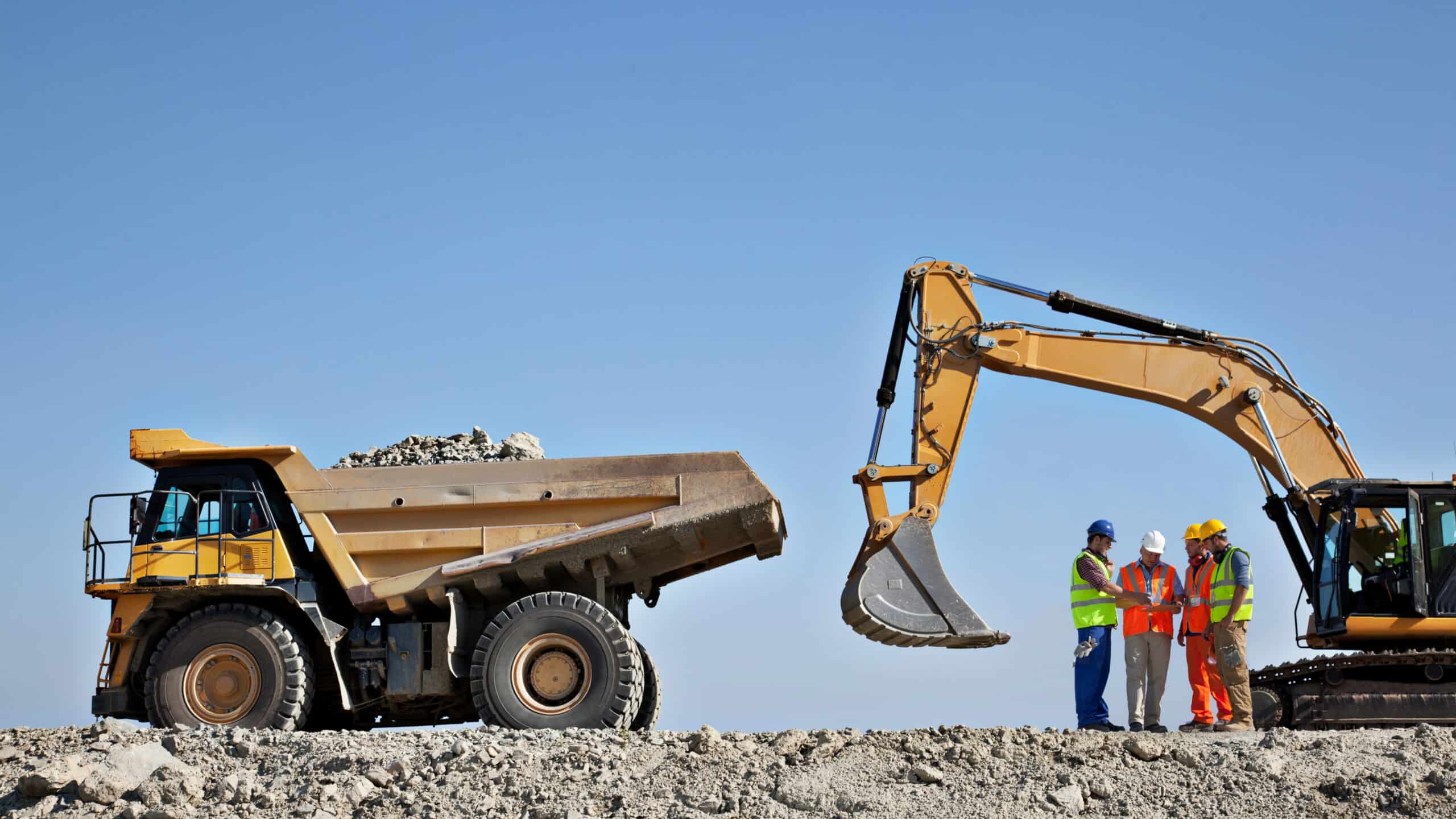 Four miners discussing with each other next to mining machinery.