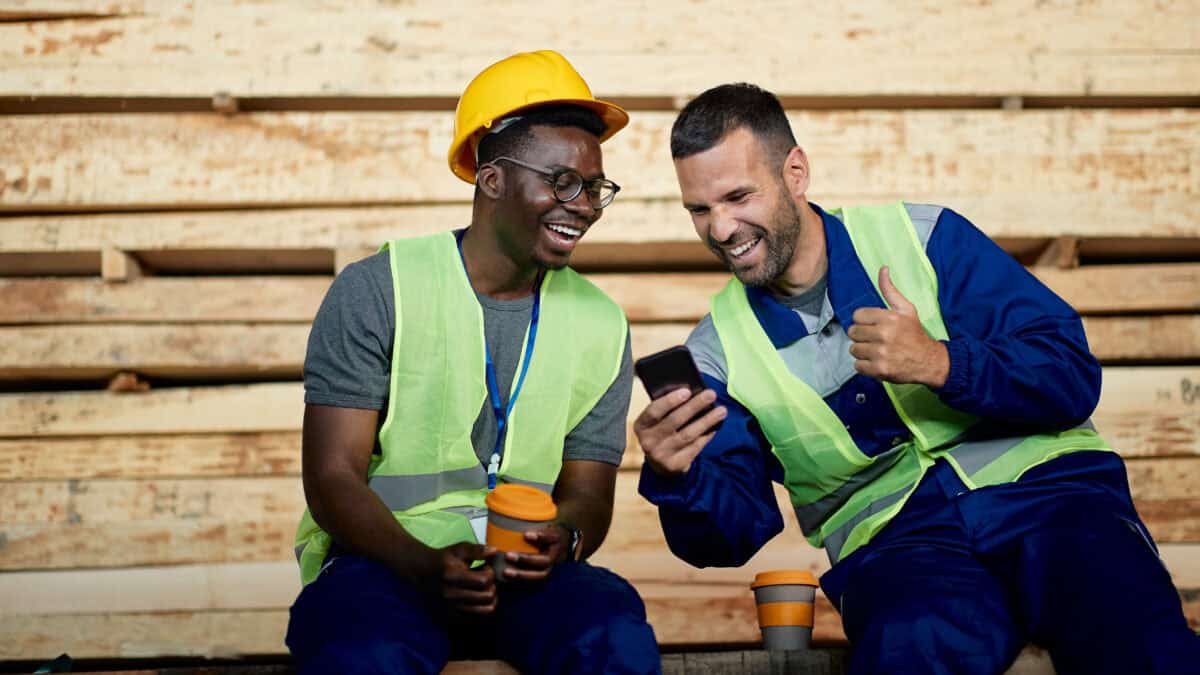Two miners laughing and having fun while using smart phone during their coffee break.