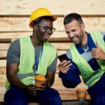 Two miners laughing and having fun while using smart phone during their coffee break.