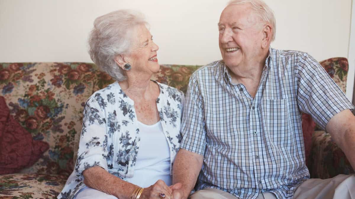 Happy senior couple sitting together hand in hand on the sofa.