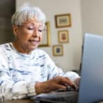Elderly woman typing on a laptop.