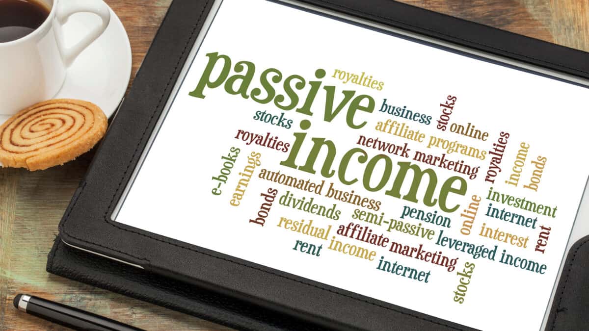 Passive income word cloud on a digital tablet, with a cup of coffee and biscuit at the side.