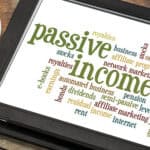 Passive income word cloud on a digital tablet, with a cup of coffee and biscuit at the side.
