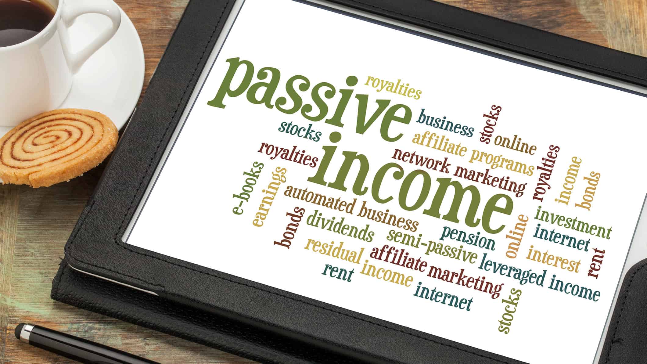 Passive income word cloud on a digital tablet, with a cup of coffee and biscuit at the side.