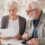 Elderly senior couple counting funds on calculator.