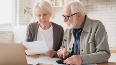 Elderly senior couple counting funds on calculator.