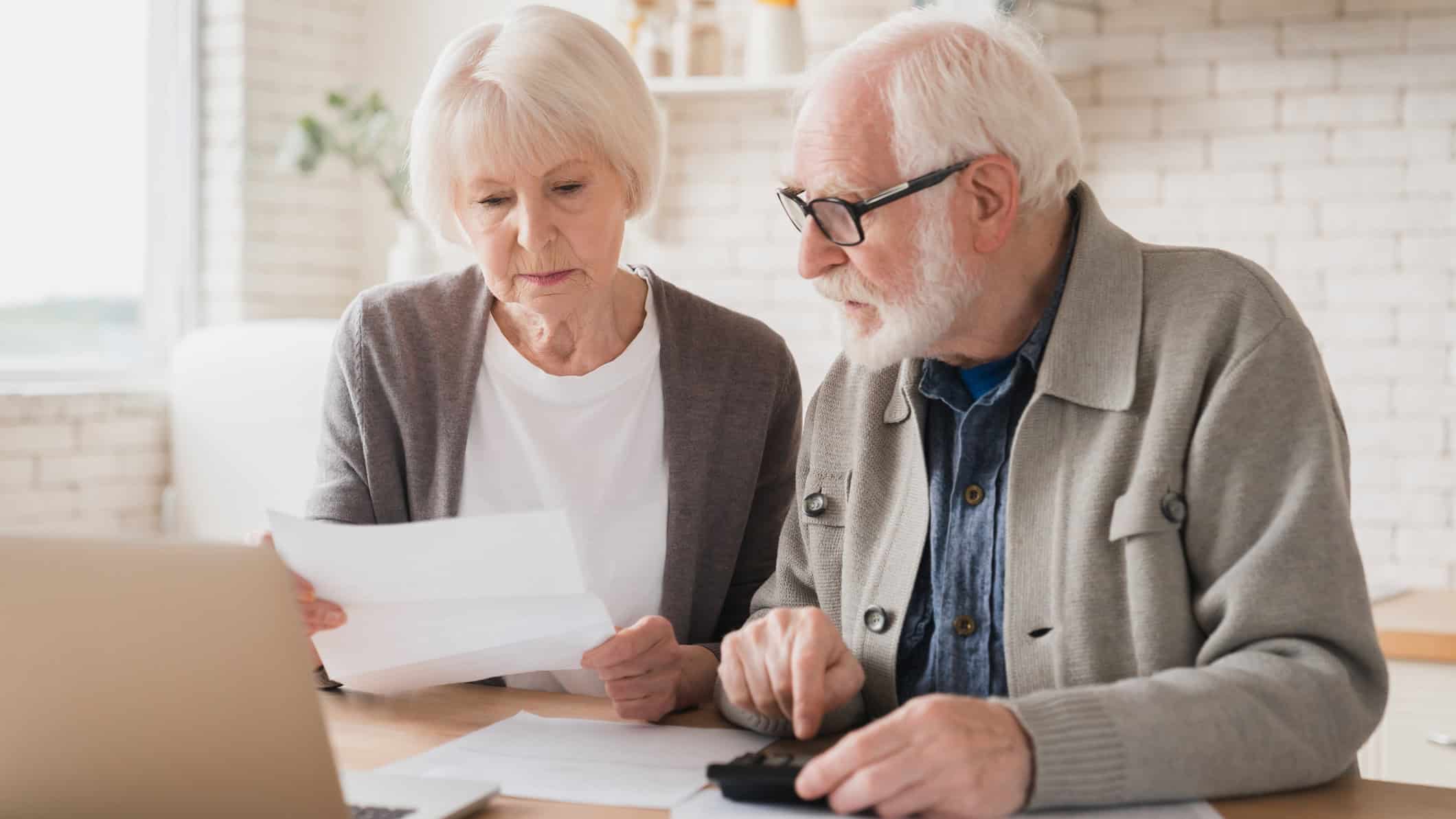 Elderly senior couple counting funds on calculator.