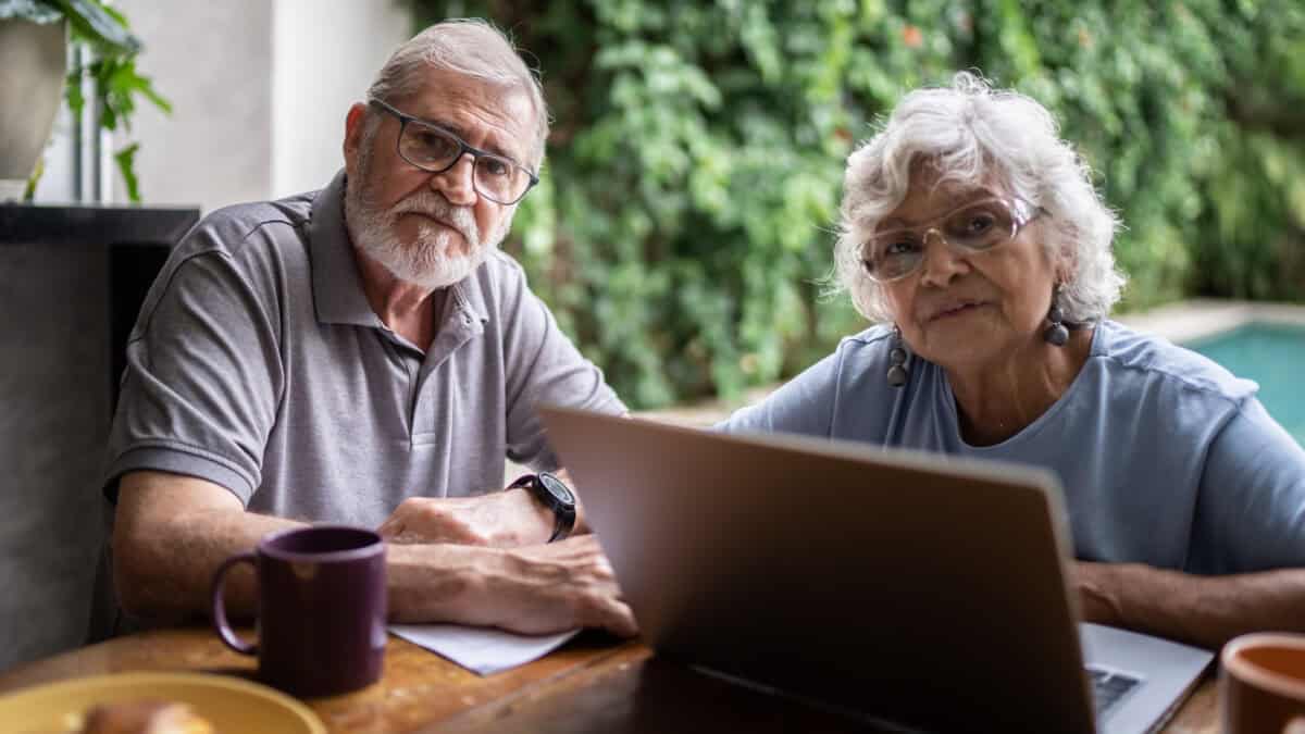 Couple looking ahead with laptop open at a table.