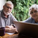 Couple looking ahead with laptop open at a table.