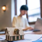 Person on his laptop with small wooden house on the table.