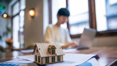 Person on his laptop with small wooden house on the table.
