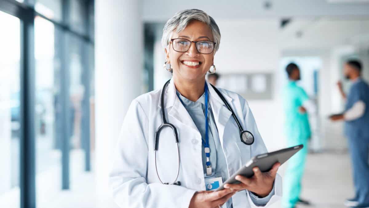 Doctor with stethoscope holding a tablet and smiling.