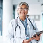Doctor with stethoscope holding a tablet and smiling.