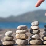Hand stacking increasing piles of rocks.