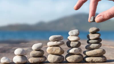 Hand stacking increasing piles of rocks.